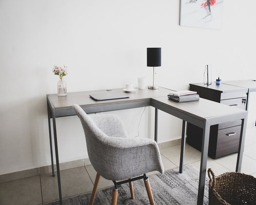 An organized clean workspace with an empty wooden table and adjustable chair next to a bright window